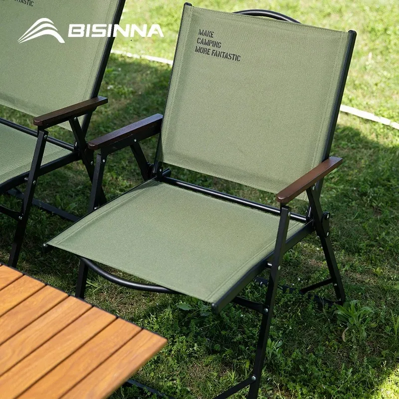 Folding camping chair with wood armrests and cushioned seat, set up at a campsite